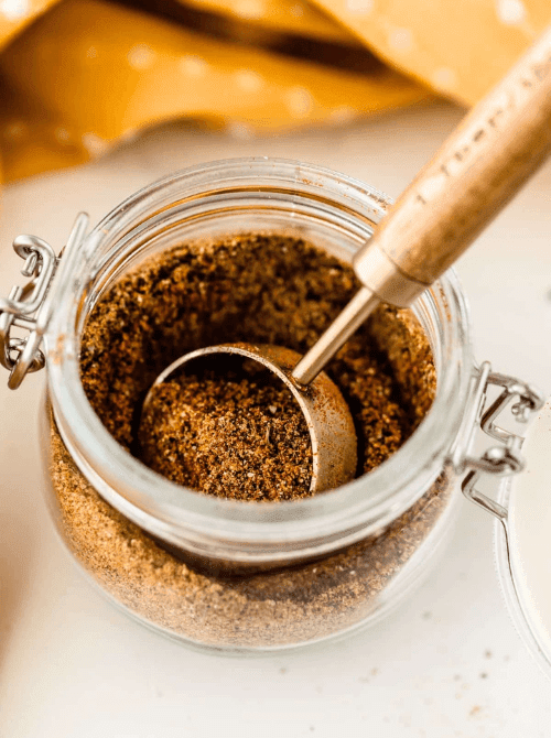 Jar of homemade pumpkin spice blend with measuring scoop, a warm and aromatic mason jar recipe that makes a simple DIY Christmas gift.