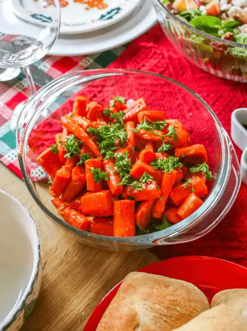 Glazed carrots garnished with fresh parsley in a glass serving bowl on a holiday table—an easy, colorful choice for Budget-Friendly Thanksgiving Vegetable Sides.