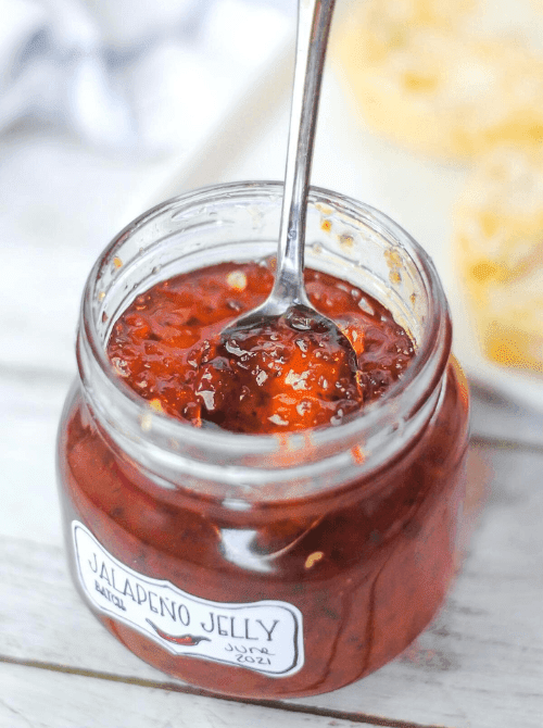 Homemade jalapeño jelly in a mason jar with spoon, a sweet and spicy mason jar recipe that makes a unique DIY Christmas gift.