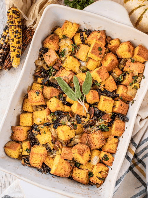 Baking dish of golden brown cornbread stuffing with herbs, onions, and bacon, a savory budget-friendly Thanksgiving side.S