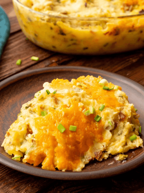Serving of loaded mashed potatoes topped with melted cheddar cheese and chives on a brown plate, featured in Budget-Friendly Thanksgiving Sides and Easy Potato Recipes for a hearty holiday dish.S