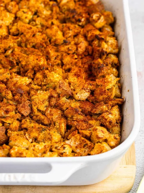 White baking dish filled with golden brown Jiffy cornbread dressing, a crispy and comforting budget-friendly Thanksgiving side.