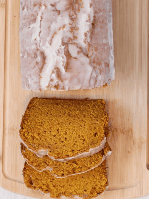 Moist pumpkin bread loaf with a sweet glaze, sliced and served on a wooden cutting board, perfect for using up leftover pumpkin puree in a simple fall dessert.