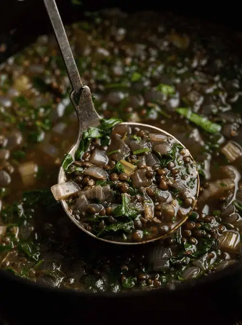 Ladle of hearty lentil and vegetable soup lifted from a pot—warm, comforting, and perfect make-ahead Halloween party food with a spooky “pond scum” twist.