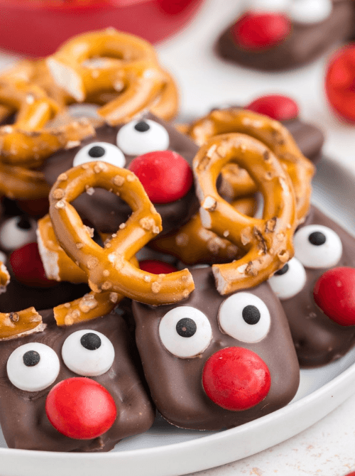 Homemade pretzel reindeers decorated with chocolate, candy eyes, and red noses, a whimsical DIY Christmas gift and easy edible holiday gift idea.