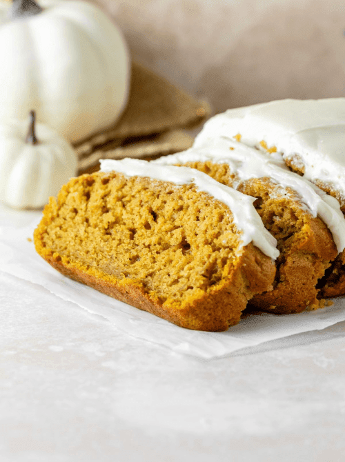 Moist pumpkin bread loaf topped with a thick layer of creamy white frosting, sliced to reveal its soft texture — a sweet and festive way to use leftover pumpkin puree for an easy fall dessert.
