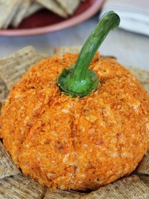 Pumpkin-shaped cheese ball coated in crushed chips and topped with a bell pepper stem, surrounded by crackers—perfect make-ahead Halloween party food that's festive and fun for entertaining.