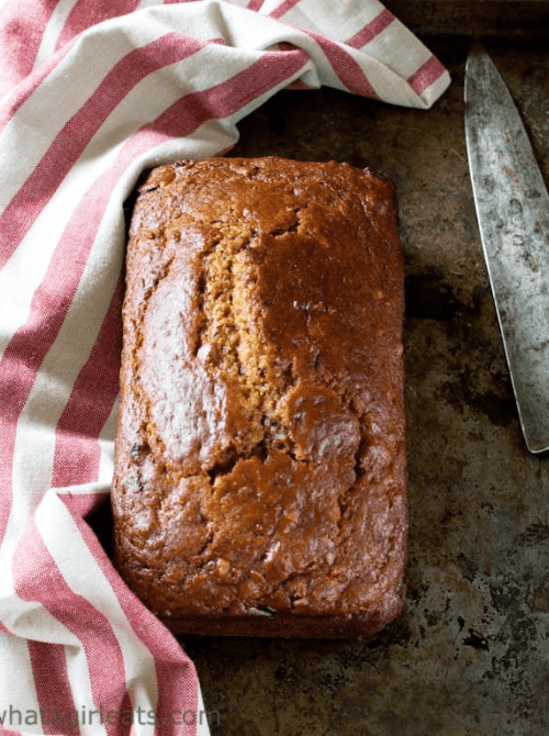 Whole loaf of pumpkin bread on a rustic baking sheet beside a red and white striped kitchen towel and knife — a classic example of what to do with leftover pumpkin puree and a staple choice for easy pumpkin bread recipes.