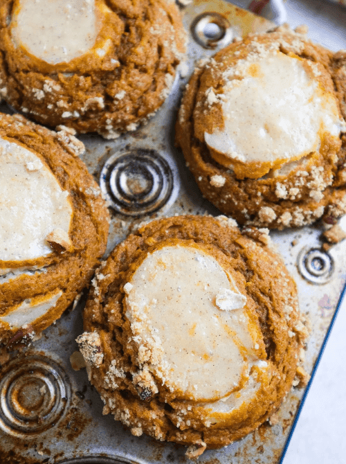 "Freshly baked pumpkin cream cheese muffins in a muffin tin, topped with a swirl of creamy filling and sprinkled with crumbly streusel for a cozy fall treat made with leftover pumpkin puree.