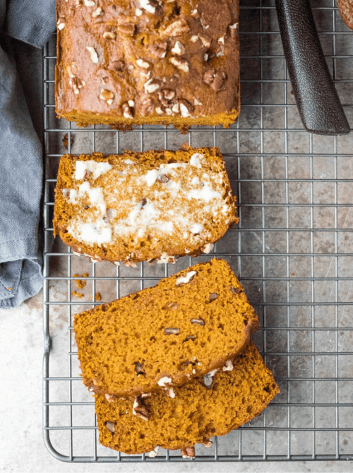 Sliced pumpkin bread with pecans cooling on a wire rack, one slice topped with melted butter — a flavorful example of what to do with leftover pumpkin puree and a nutty twist on easy pumpkin bread recipes.