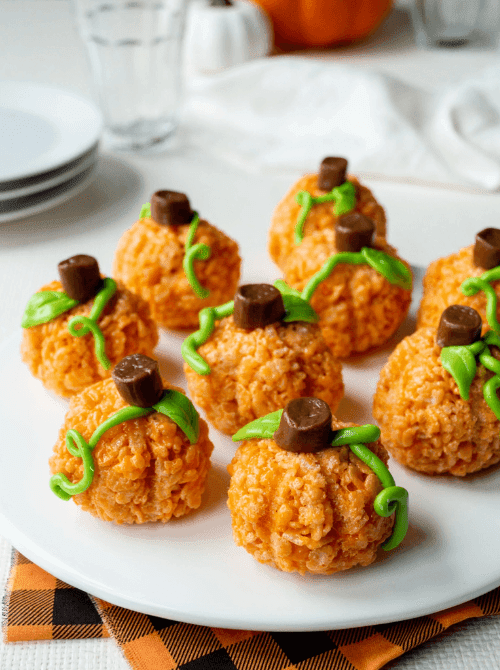 Pumpkin-shaped Rice Krispie treats decorated with green frosting vines and Rolos as stems—playful and colorful make-ahead Halloween party food for kids and fall gatherings.