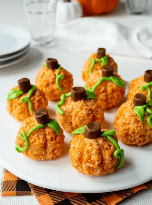 Pumpkin-shaped Rice Krispie treats decorated with green frosting vines and Rolos as stems—playful and colorful make-ahead Halloween party food for kids and fall gatherings.