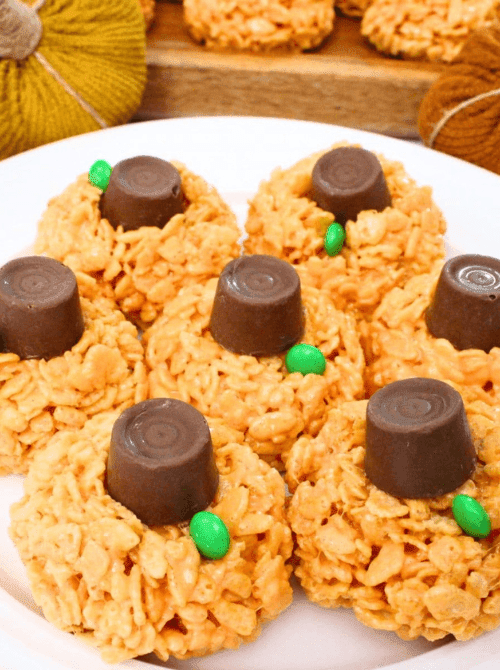 Pumpkin-shaped Rice Krispie treats topped with Rolos and green candies to resemble stems—fun and festive make-ahead Halloween party food that’s perfect for kids.