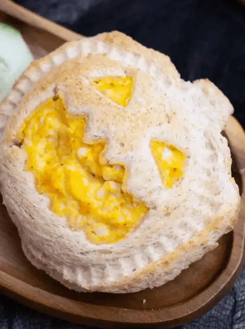 Jack-o'-lantern shaped sandwich filled with creamy egg salad, served on a wooden plate—festive and fun make-ahead Halloween party food for kids and themed lunches.