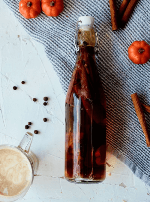 Homemade pumpkin spice extract in a glass bottle with cinnamon sticks and spices, a fragrant mason jar recipe and festive DIY Christmas gift idea.