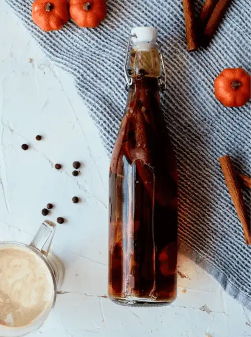 Homemade pumpkin spice extract in a glass bottle with cinnamon sticks and spices, a fragrant mason jar recipe and festive DIY Christmas gift idea.