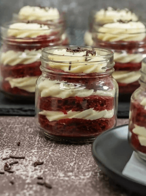 Individual red velvet jar cakes layered with cream cheese frosting, a festive DIY Christmas gift and easy edible gift idea for holiday celebrations.