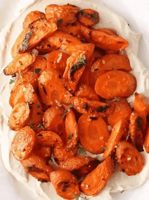 Roasted carrots served over whipped feta and topped with fresh herbs—an elegant yet simple option for Budget-Friendly Thanksgiving Vegetable Sides.