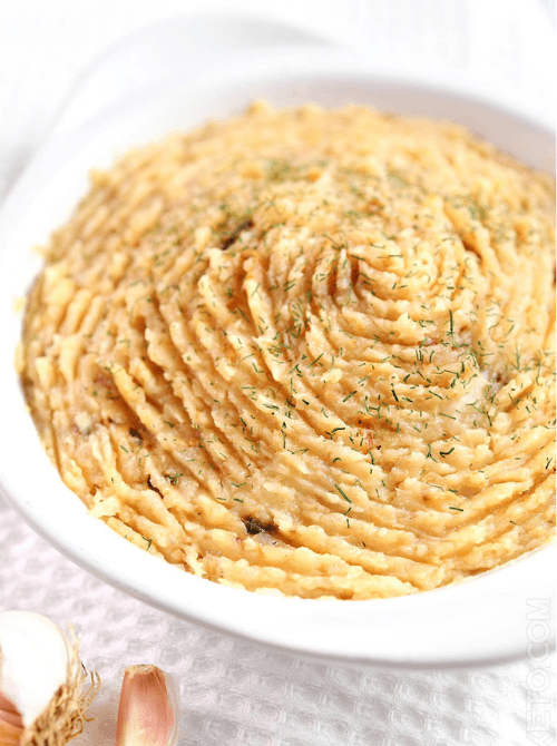 Mashed roasted turnips with garlic in a white dish, topped with herbs—an easy, low-carb alternative for Budget-Friendly Thanksgiving Vegetable Sides.