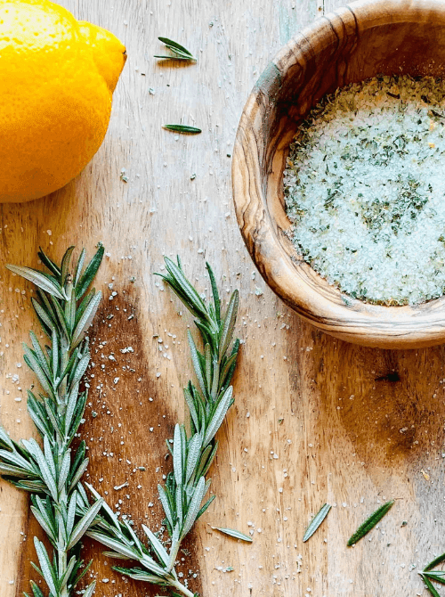 Homemade rosemary lemon herb salt in a wooden bowl with fresh rosemary and lemon, a flavorful mason jar recipe perfect for DIY Christmas gifts.
