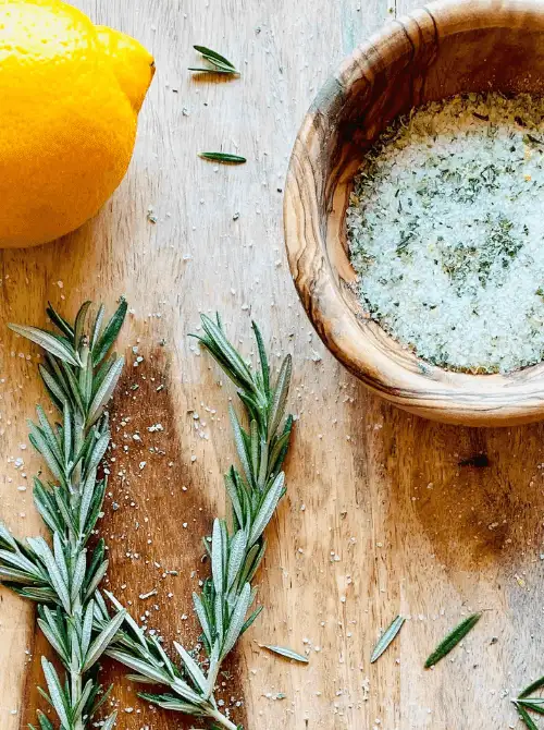 Homemade rosemary lemon herb salt in a wooden bowl with fresh rosemary and lemon, a flavorful mason jar recipe perfect for DIY Christmas gifts.
