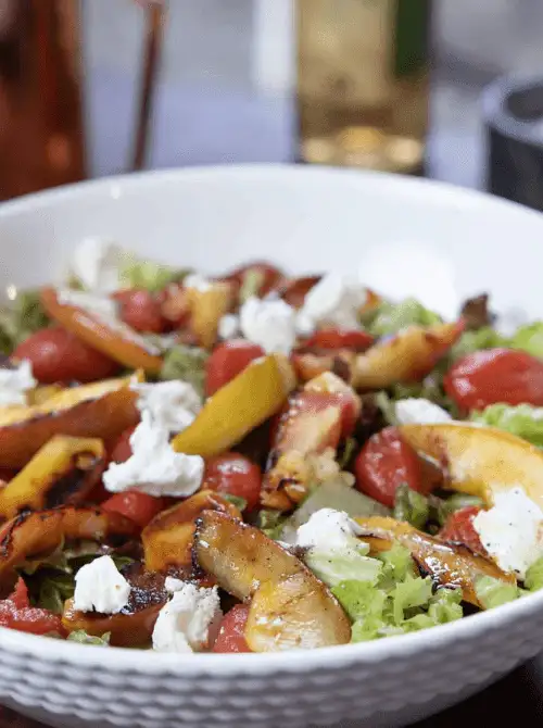Warm salad with seared apples, cherry tomatoes, and goat cheese in a white bowl—an elegant and flavorful option for Budget-Friendly Thanksgiving Vegetable Sides.