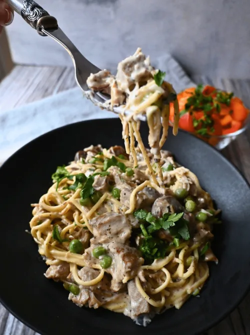 Creamy turkey tetrazzini with pasta, mushrooms, and peas served in a black bowl — a comforting idea for what to make with Thanksgiving leftovers and one of the best easy turkey recipes for family dinners.