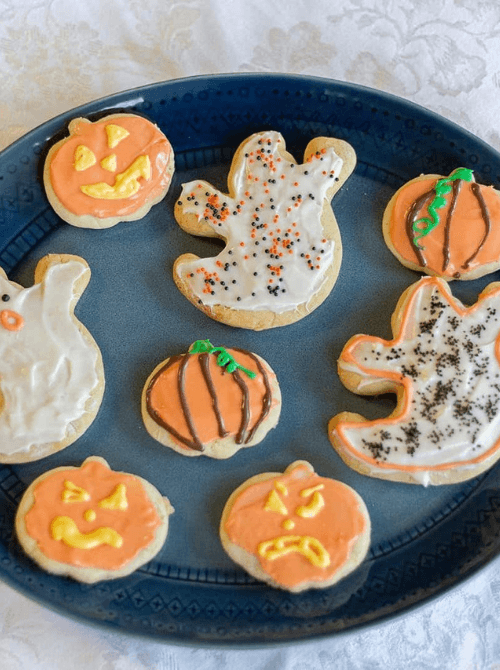 Frosted Halloween sugar cookies in pumpkin and ghost shapes—easy make-ahead party treats decorated with colorful icing and sprinkles for a festive vibe.