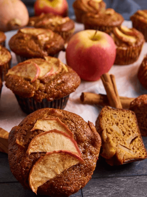 Freshly baked apple-topped pumpkin muffins arranged with whole apples and cinnamon sticks — a seasonal idea for what to do with leftover pumpkin puree and a fruity variation on easy pumpkin bread recipes.