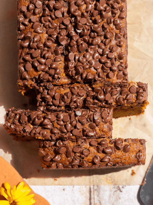 Top view of sliced pumpkin bread covered in a generous layer of chocolate chips on parchment paper — a decadent example of what to do with leftover pumpkin puree and a rich variation for easy pumpkin bread recipes.