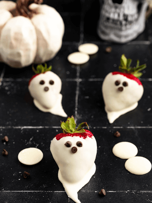No-Bake Halloween Treats featuring white chocolate-dipped strawberries decorated to look like ghosts with mini chocolate chip eyes, set against a spooky party backdrop.