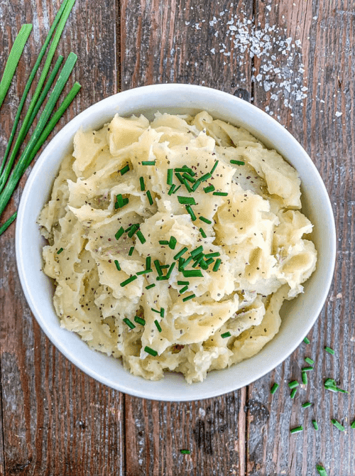 Bowl of creamy mashed potatoes garnished with fresh chives on a rustic wooden table, part of Budget-Friendly Thanksgiving Sides and Easy Potato Recipes for a classic holiday favorite.