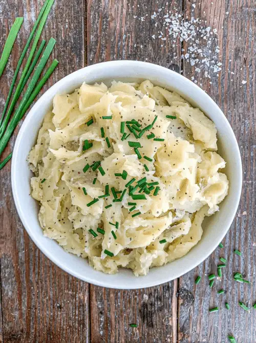 Bowl of creamy mashed potatoes garnished with fresh chives on a rustic wooden table, part of Budget-Friendly Thanksgiving Sides and Easy Potato Recipes for a classic holiday favorite.