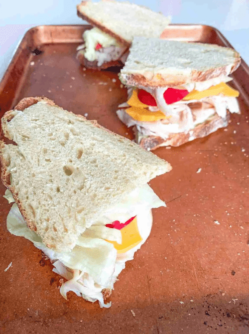 Stacked turkey sandwiches with cheddar cheese, lettuce, and tomato on sourdough bread — a simple idea for what to make with Thanksgiving leftovers and one of the best easy turkey recipes for a quick meal.