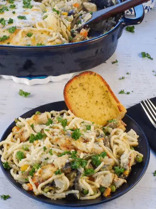 Plate of baked turkey tetrazzini with noodles, peas, carrots, and melted cheese, served with garlic bread — a hearty idea for what to make with Thanksgiving leftovers and one of the best easy turkey recipes for a family meal.