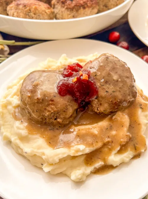 Savory meatballs served over mashed potatoes with gravy and cranberry sauce – a hearty idea for what to make with Thanksgiving leftovers and recipes that stretch your budget.