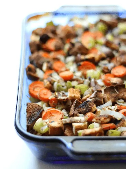 Glass baking dish filled with colorful vegetable stuffing made with carrots, celery, and bread cubes, a hearty budget-friendly Thanksgiving side.