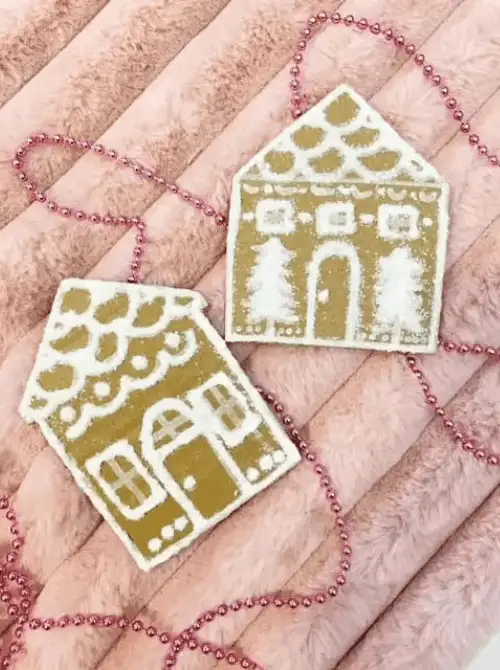 Dollar Store Christmas DIY decor gingerbread house ornaments made from cardboard with white painted details, displayed with pink bead garland.