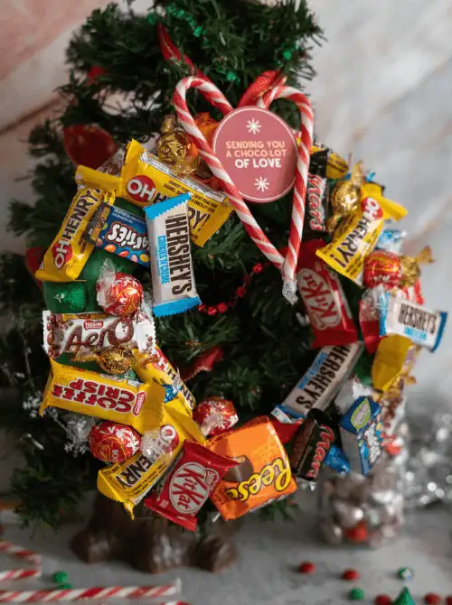 Dollar Store Christmas DIY decor candy wreath made with chocolate bars, Reese’s, KitKat, and candy canes, displayed on a Christmas tree.