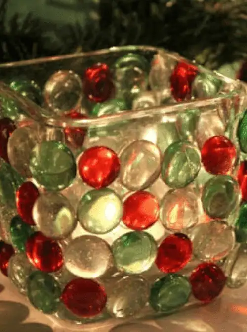 Dollar Store Christmas DIY decor candle holder made from a glass vase decorated with red, green, and clear gem stones for a festive holiday glow.