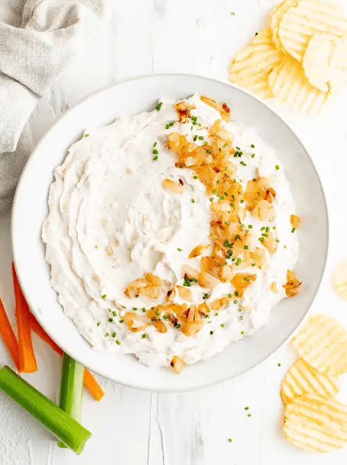 Homemade French onion dip topped with caramelized onions and chives, served with potato chips and fresh veggies—an irresistible pick for Party Dips for the Holidays and Cheesy Dips.