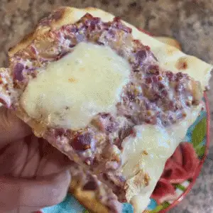 Close-up of a slice of Oktoberfest sauerkraut pizza topped with caramelized onions, apples, and melted cheese on a crispy crust.