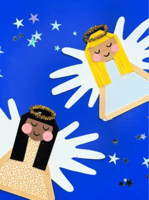 Dollar Store Christmas DIY decor angel crafts made with handprint wings, popsicle stick bodies, paper dresses, and gold pipe cleaner halos, displayed on a blue starry background.