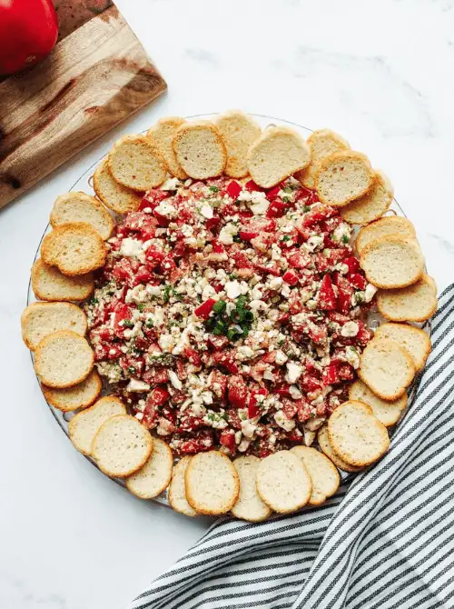 Tomato feta dip topped with herbs and surrounded by toasted baguette slices, a colorful option for Party Dips for the Holidays and Cheesy Dips.