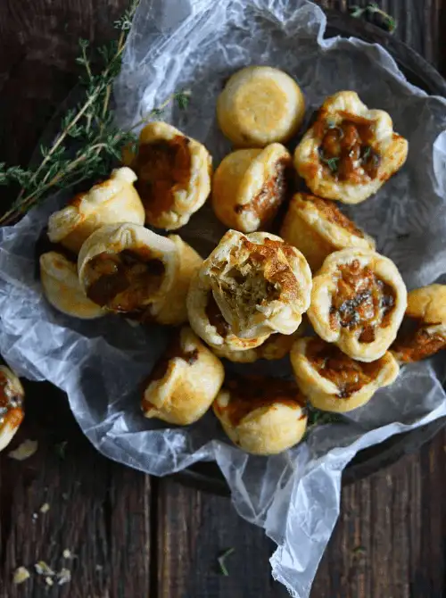 Caramelized Onion Tartlets baked in golden puff pastry — a rich and elegant appetizer for Christmas party food ideas, featuring sweet onions and thyme in bite-sized cups, perfect for budget-friendly holiday entertaining and easy finger food appetizers for a crowd.