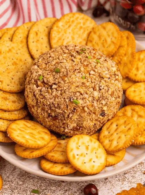 Classic cheese ball coated in chopped nuts surrounded by crackers, a simple and delicious option for make-ahead Christmas appetizers and crowd-pleasing Christmas party food ideas.