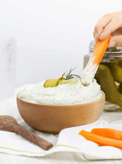 Creamy dill pickle dip with cream cheese, garnished with fresh dill and pickles, served with carrot sticks, a tangy option for Party Dips for the Holidays with Unique Twists.
