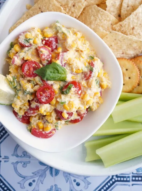 Easy tofu corn dip with cherry tomatoes, corn, and herbs served with crackers, tortilla chips, and celery, a vibrant pick for Party Dips for the Holidays with Unique Twists.