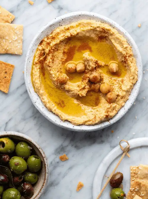 Classic garlic hummus drizzled with olive oil and sprinkled with paprika, served with olives and crackers, a flavorful pick for Party Dips for the Holidays with Global Twists.