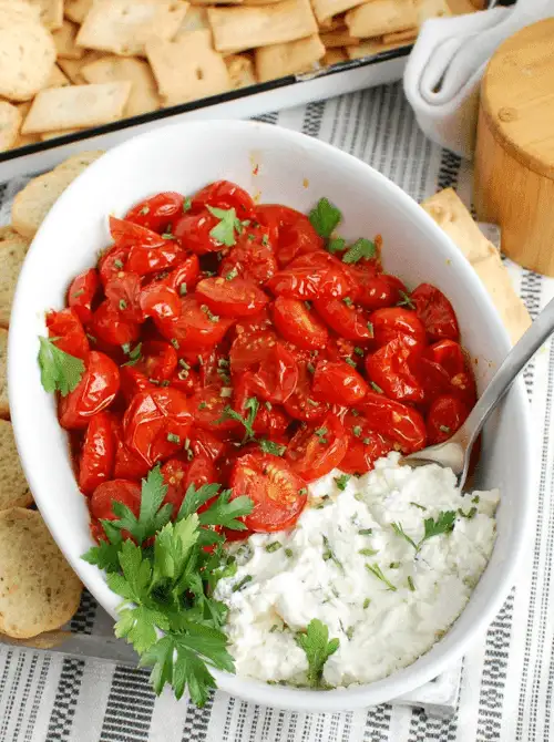 Goat cheese and roasted tomato dip served in a white bowl with fresh herbs and crackers, a flavorful choice for make-ahead Christmas appetizers and festive Christmas party food ideas.